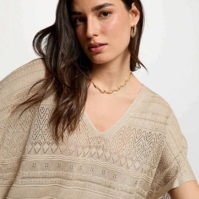 Mulher com blusa bege de malha rendada e joias douradas