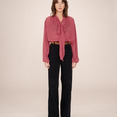 Mulher com blusa rosa de gola laço e calças pretas de cintura alta.