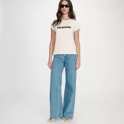 Mulher a usar t-shirt creme com texto Ristretto, jeans azuis largos e sandálias brancas.