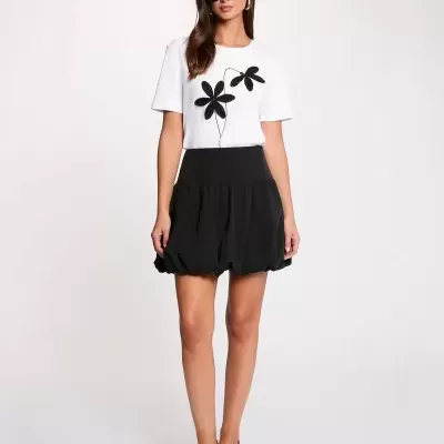 Mulher com t-shirt branca de manga curta com flores pretas e saia preta rodada