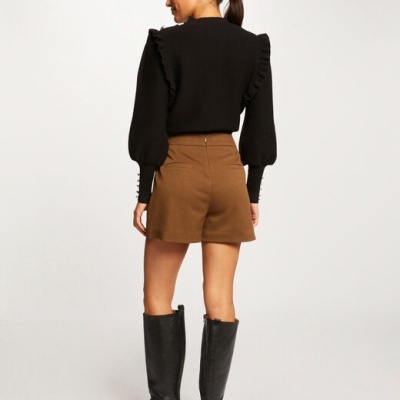 Mulher de costas com camisola preta, calções castanhos e botas pretas