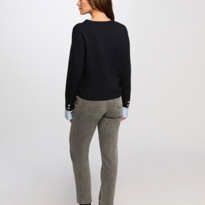 Mulher de costas com camisola preta, camisa azul, jeans cinza e botins pretos