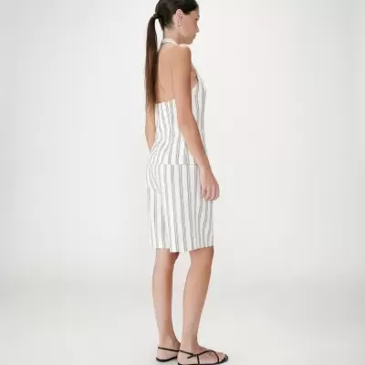 Mulher vestindo conjunto branco com riscas verticais cinzentas e sandálias pretas.