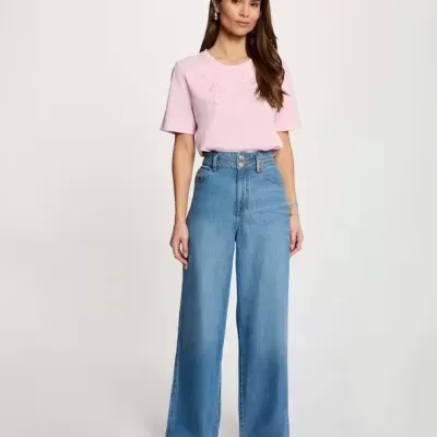 Mulher com t-shirt rosa e jeans azul de perna larga em fundo branco