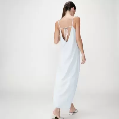 Mulher de costas com vestido comprido branco e alças finas, em fundo branco