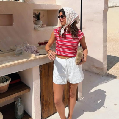 Mulher com roupa casual de verão, incluindo top riscado vermelho e branco, calções brancos, lenço floral e sapatos vermelhos