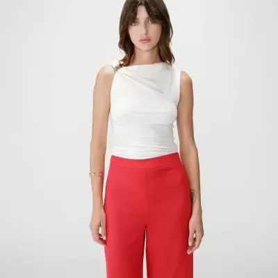 Mulher com top branco e calças vermelhas em fundo branco