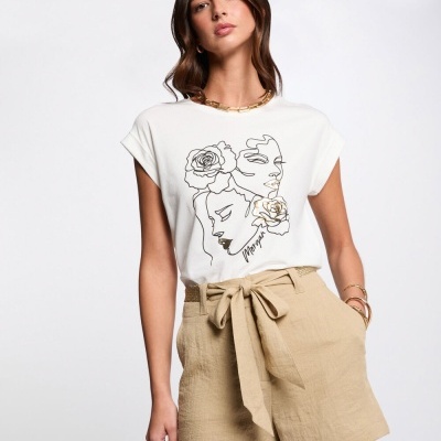 T-shirt branca com estampa artística de dois rostos e flores, calções bege com laço numa modelo sobre fundo branco.