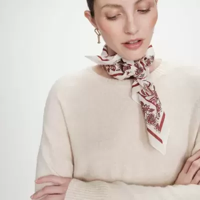 Mulher com lenço floral vermelho e rosa amarrado ao pescoço e camisola bege de malha