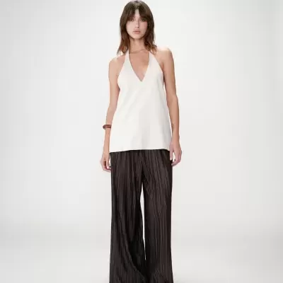 Mulher com top branco e calças largas pretas em fundo branco