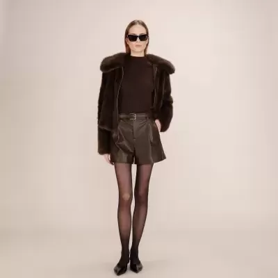 Mulher a usar casaco de pelo castanho e calções de pele castanhos com óculos escuros