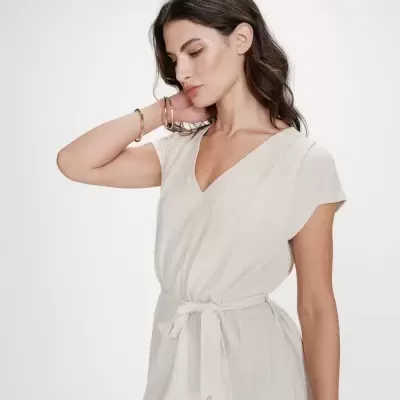 Vestido bege claro com cinto e decote em V usado por modelo com pulseiras douradas