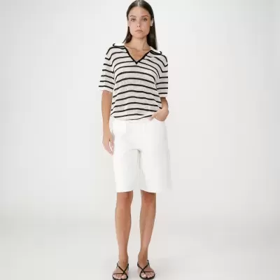 Mulher com camisola riscada, calções brancos e sandálias pretas em fundo branco