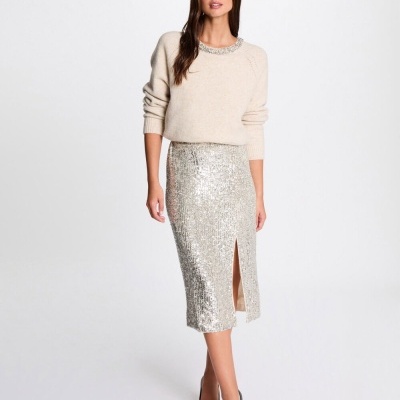 Mulher com camisola bege e saia prateada midi com lantejoulas e corte frontal