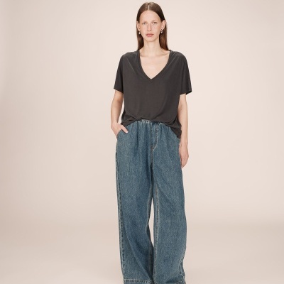 Pessoa vestindo t-shirt preta de decote em V e calças largas de ganga azul em fundo bege