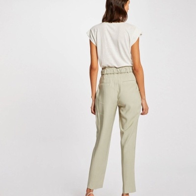 Mulher com t-shirt branca e calças bege claras vista de costas, sapatos brancos