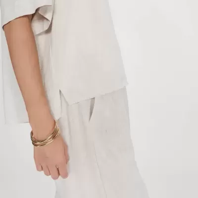 Roupa bege clara em linho com pulseiras douradas no pulso