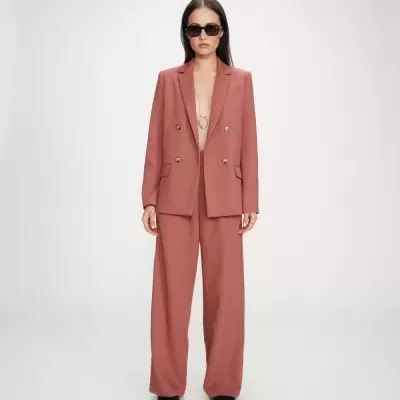 Mulher com blazer e calças largas terracota, óculos escuros e sapatos pretos.