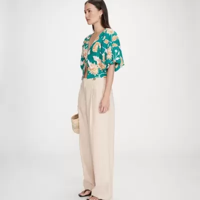 Mulher com blusa verde floral, calças largas bege, sandálias pretas e bolsa de palha