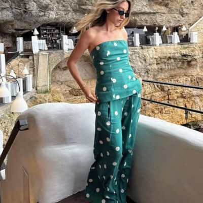 Mulher com conjunto verde de bolas brancas, top e calças largas, junto a corrimão em área com parede de pedra.