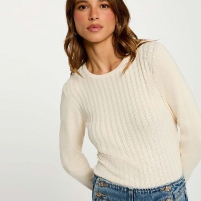 Mulher a usar blusa de malha creme e calças de ganga azul com botões