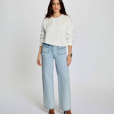 Mulher com camisola branca com bordados e jeans largos azuis