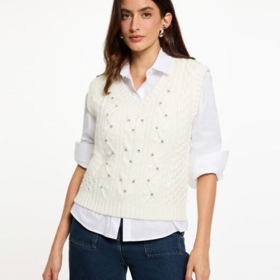 Mulher a vestir camisola de malha branca com pérolas sobre camisa branca e calças de ganga azul