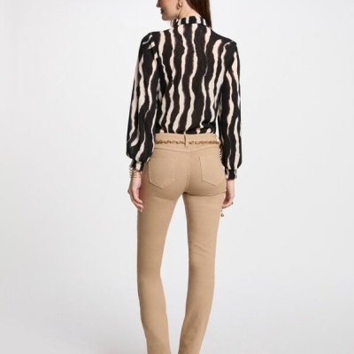 Modelo de costas usa calças bege justas com cinto dourado e blusa preta e branca com padrão animal