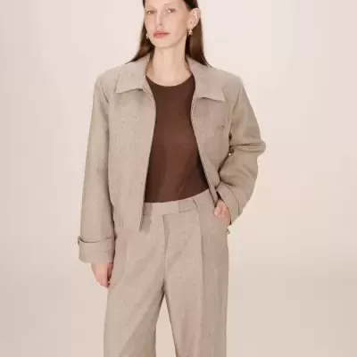 Mulher com casaco bege e calças largas bege com t-shirt castanha.