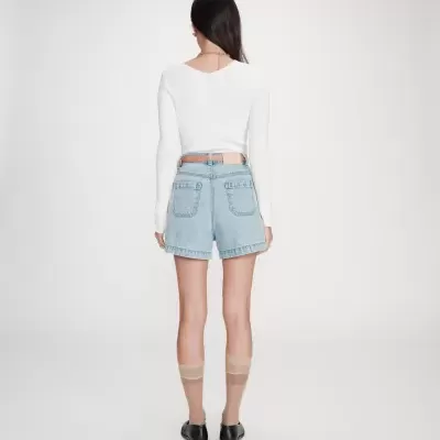 Mulher com camisola branca, calções de ganga, meias transparentes e sapatos pretos vista de costas