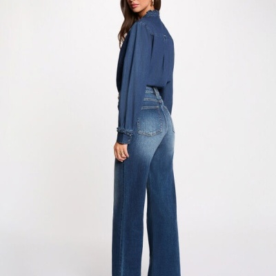 Mulher vestindo calças de ganga azuis e camisa azul escura sobre fundo branco