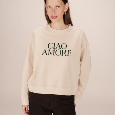 Sweat bege com texto 'CIAO AMORE' usado por mulher sobre fundo neutro