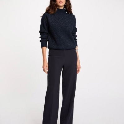 Mulher com camisola preta de gola alta e calças pretas retas em fundo branco