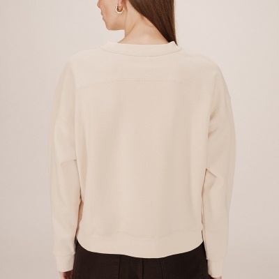 Casaco bege claro de malha visto de costas, combinado com calças pretas