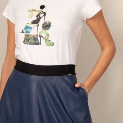 T-shirt branca com estampado colorido de sapatos e uma mala, saia azul escura e cinto preto