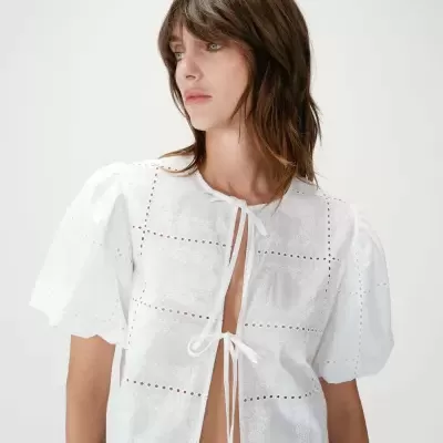 Blusa branca com bordados e mangas bufantes num fundo claro.