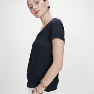 Mulher com t-shirt azul escuro de manga curta e calças brancas em fundo branco