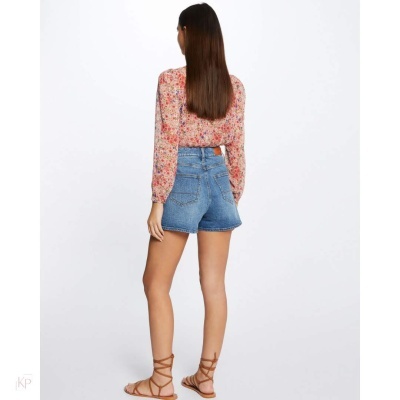 Mulher de costas com blusa floral, calções de ganga e sandálias castanhas num fundo branco.