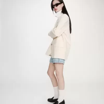 Mulher com blazer creme, calções de ganga e sapatos pretos