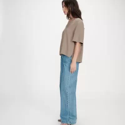 Mulher de perfil com t-shirt bege de mangas médias e calças de ganga azul claro largas