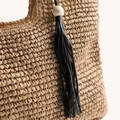 Saco de mão trançado bege com pendente de franjas pretas e conta branca