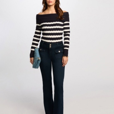 Mulher a usar camisola riscada preta e branca, calças jeans pretas e mala azul clara.