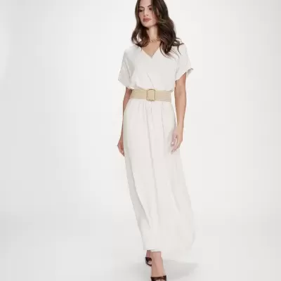 Mulher com vestido comprido branco e cinto bege em fundo branco