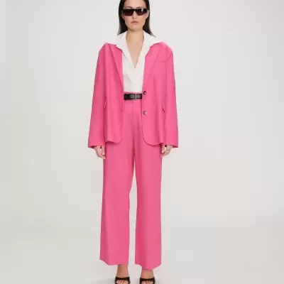 Mulher com fato rosa, camisa branca e óculos escuros em fundo branco