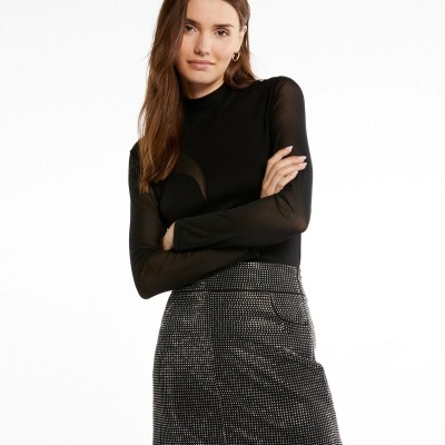 Mulher com top preto de manga comprida transparente e saia curta preta com padrão de pontos brancos.