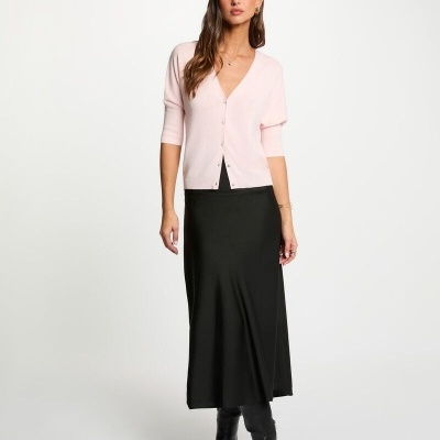 Mulher com cardigan rosa claro, saia preta e botas pretas em fundo branco