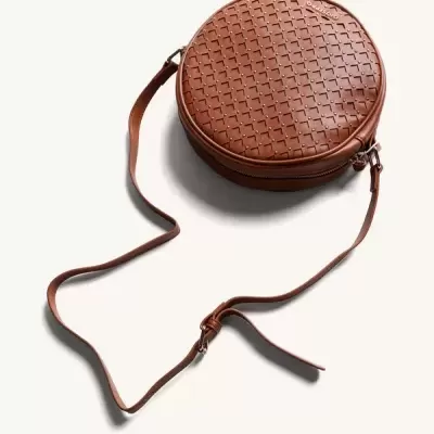 Mala redonda castanha de pele com padrão entrelaçado e alça ajustável