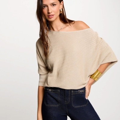 Mulher com camisola bege de malha de riscas e calças jeans escuras num fundo branco