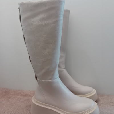 Botas altas creme de couro com sola espessa em superfície rosa.
