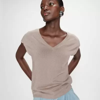 Mulher com blusa bege brilhante de mangas curtas e calças de ganga azuis em fundo branco